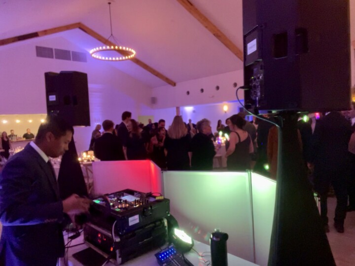 A Vermont wedding DJ sets the mood, fine-tuning equipment as guests dance and celebrate under romantic lights in a stylish venue.