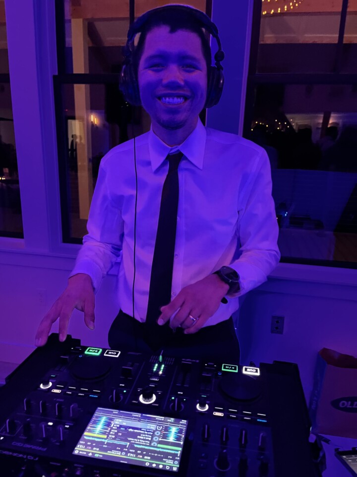 A friendly Vermont wedding DJ in a white shirt and black tie mixes tunes behind a vibrant controller, ready to light up your night.