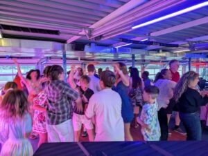 Couples and guests of all ages dance joyfully together under romantic purple and blue lights at an indoor wedding celebration, while Vermont DJ Aaron Carroll creates an unforgettable, energetic atmosphere perfect for your special day.